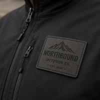 High-quality black custom leather patch with debossed Northbound Outdoor Co. logo, precision-stitched onto a black waterproof technical jacket for premium apparel branding.