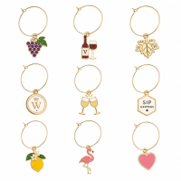 Personalized wine glass charms featuring grape, wine bottle, leaf, flamingo, lemon, heart, and logo designs with gold-tone wire rings and enamel color accents.