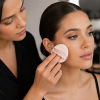 Makeup artist applying foundation with powder puff on model, professional cosmetic application tool