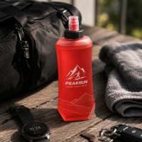 Custom red running soft flask featuring a screen-printed trail running logo, displayed next to a gym bag and fitness watch for sports brand merchandising.